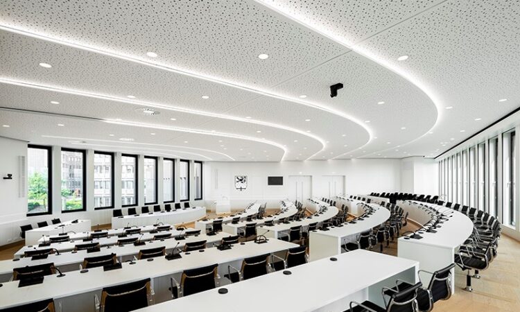 Auch die gestalterischen Fähigkeiten der Gipskartondecke kommen im großen Sitzungsaal eindrucksvoll zum Tragen: So wird der stufenweise Anstieg der Sitzreihen durch den treppenartigen Verlauf der Klimadecke eindrucksvoll aufgegriffen. Bildquelle: QLIMATE GmbH, Lahr